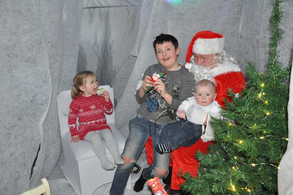 Logan Young joins six month old Alfaigh Lambie on Santa's knee at Corrie while Allaigh Lambie sets to work on her cupcake