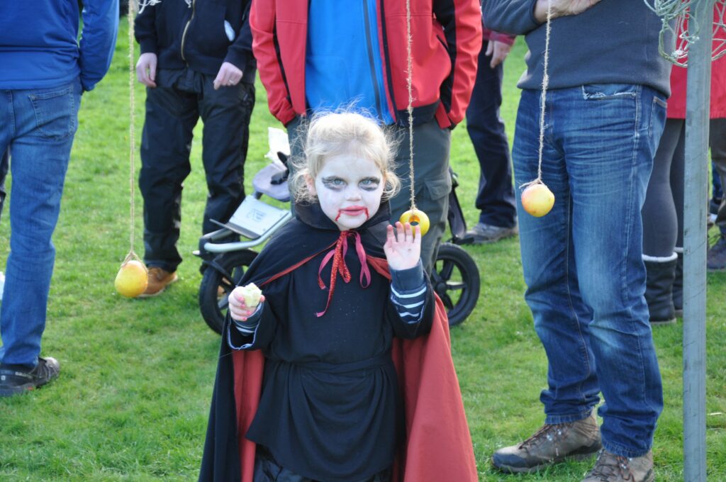 A young girl dressed up as a vampire waves to the camera after bobbing for apples.