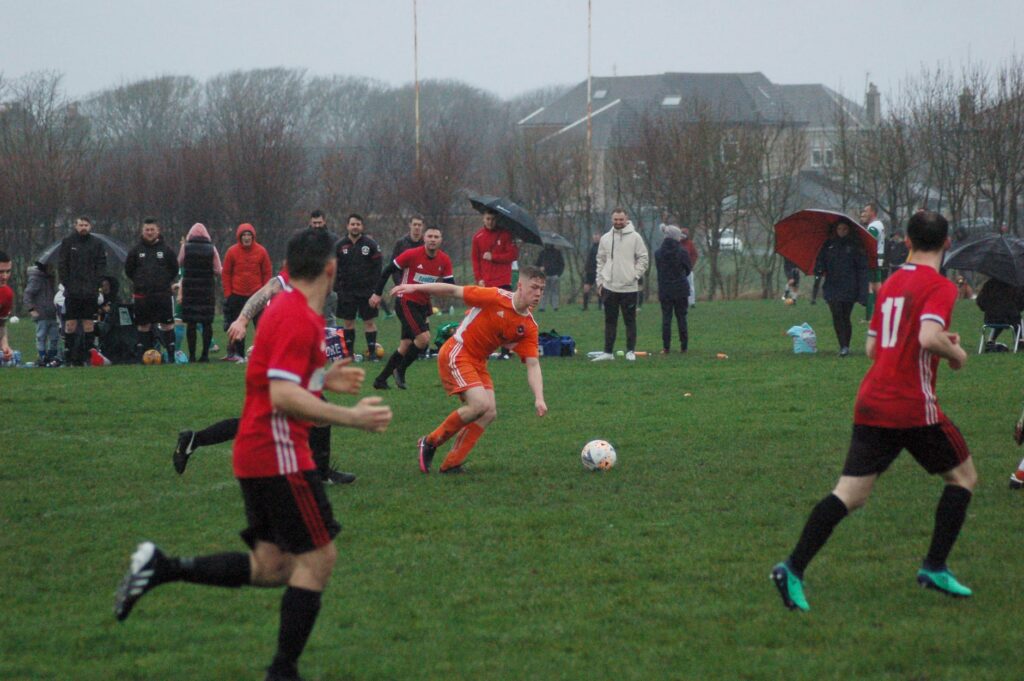 Spectators shield from the rain as Arran player Kieran Rae claims possession of the ball.
