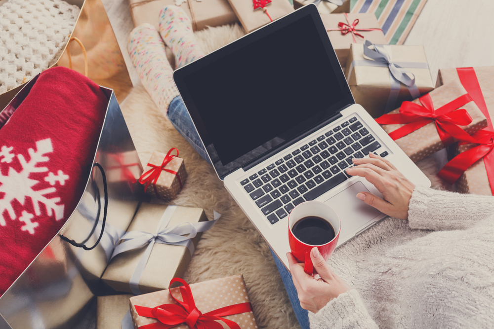 Christmas Shopping tips. Woman typing on laptop, surrounded by wrapped gifts