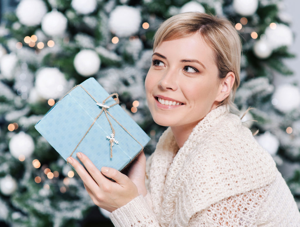 Lady holding xmas gift by the tree Pic: Istockphoto