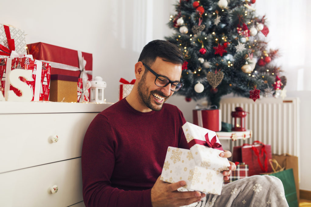 Smiling young man opening Christmas gift at home Pic: Istockphoto