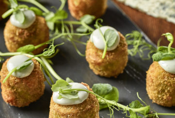 Tray of small, round breadcrumbed croquettes, each with a blob of Saint Agur blue cheese puree, decorated with pea shoots