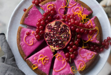 Gingerbread cake with bright pink icing, cut into 8 pieces, decorated with orange zest, berries and pomegranate seeds