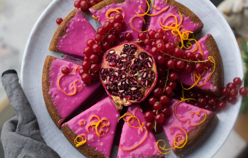 Gingerbread cake with bright pink icing, cut into 8 pieces, decorated with orange zest, berries and pomegranate seeds