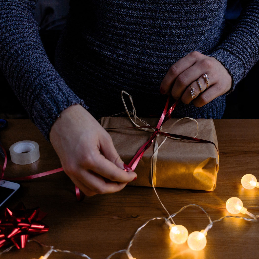 Person tying ribbon around brown paper parcel, fairy lights in foreground