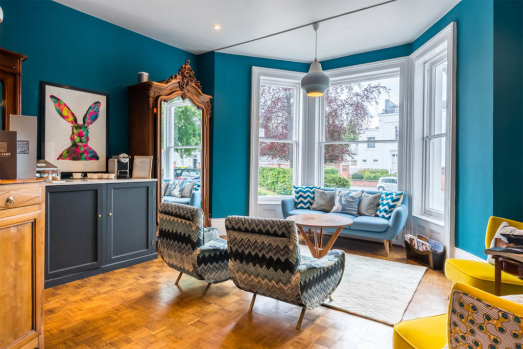 Reception area at The Town House, teal walls, warm honey flooring, funky sofa in traditional bay window