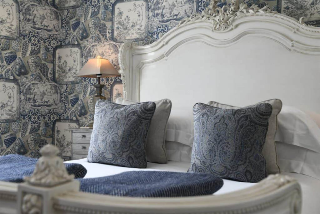 Ornate cream-painted wooden bed headboard with cream and dusky blue cushions and wallpaper, Padstow Town House hotel