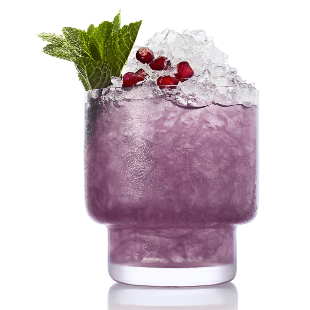 Glass filled with crushed ice and purple drink, garnished with mint and berries