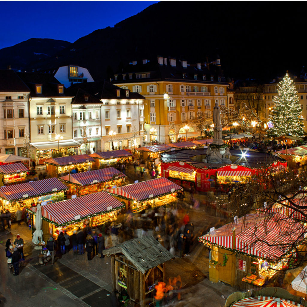 White and yellow painted buildings surround the square full of stalls with red and white striped canopies, hills behind silhouetted against the night sky