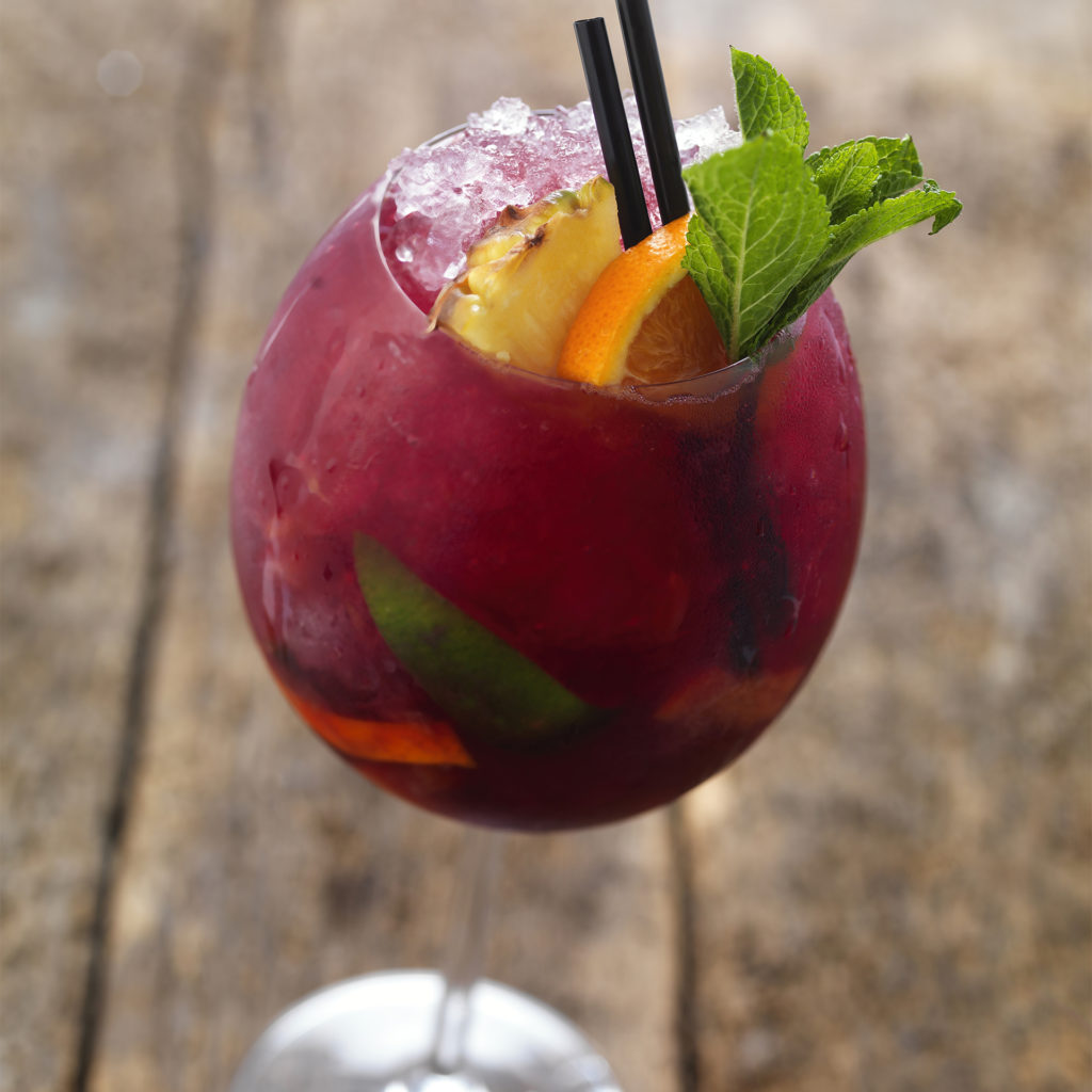 Glass of red coloured mocktail with citrus slices and mint garnish