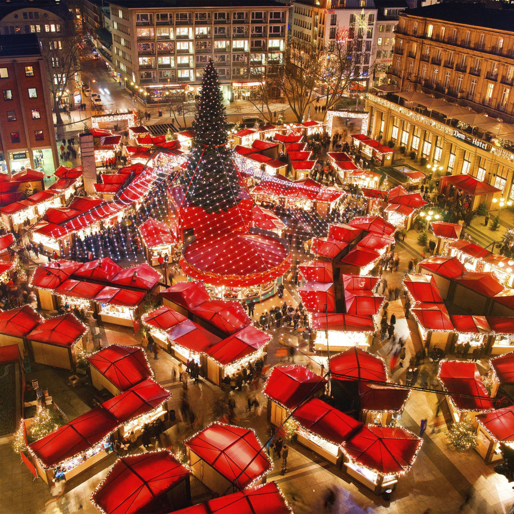 Aerial view of fairylit, red-roofed market stalls in square around giant Christmas tree