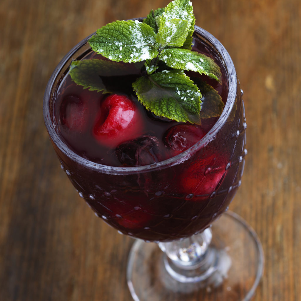 Deep red mocktail with ice, raspberry and mint garnish
