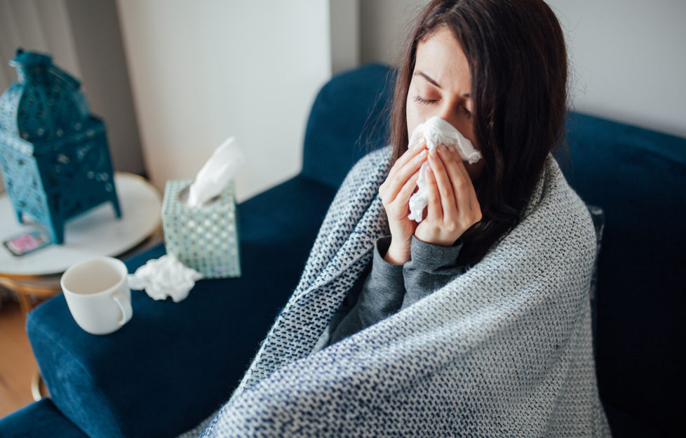 Sick woman blowing her nose, she covered with blanket