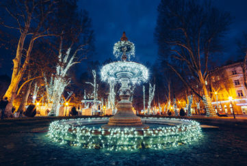 Fairylit fountain at night, trees and floodlit classical architecture