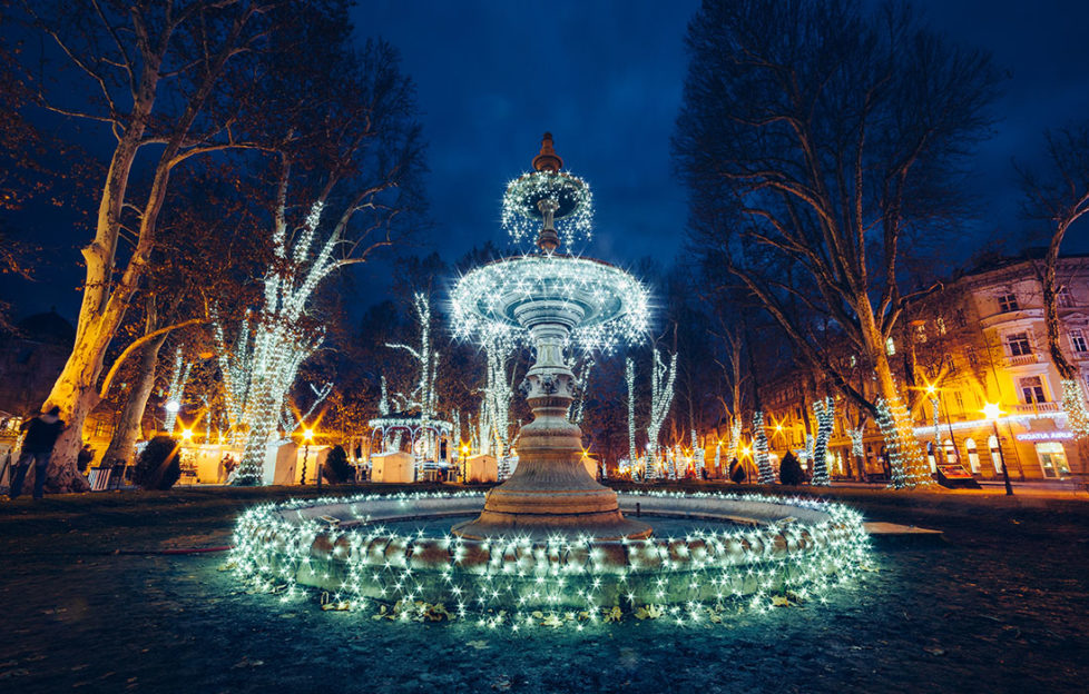 Fairylit fountain at night, trees and floodlit classical architecture