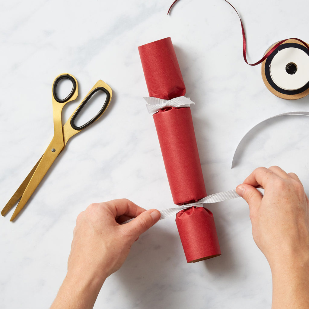 Tying ribbon around paper tube, either side of central cardboard tube, to make a recognisable cracker.