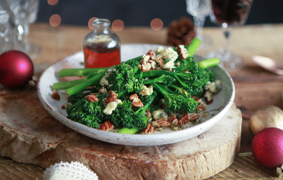 Broccoli, pecans and blue cheese on a serving plate with small glass jar of maple dressing, all on board made of a slice of tree trunk