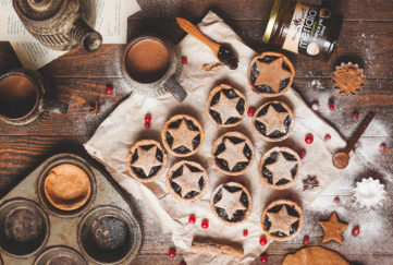 10 star-topped mince pies, cranberries scattered over, cinnamon stick, jar of Meridian almond butter, earthenware teapot and mug of tea on side