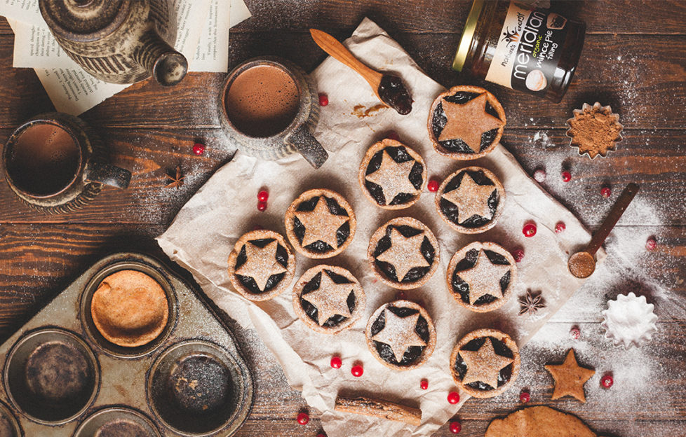 10 star-topped mince pies, cranberries scattered over, cinnamon stick, jar of Meridian almond butter, earthenware teapot and mug of tea on side