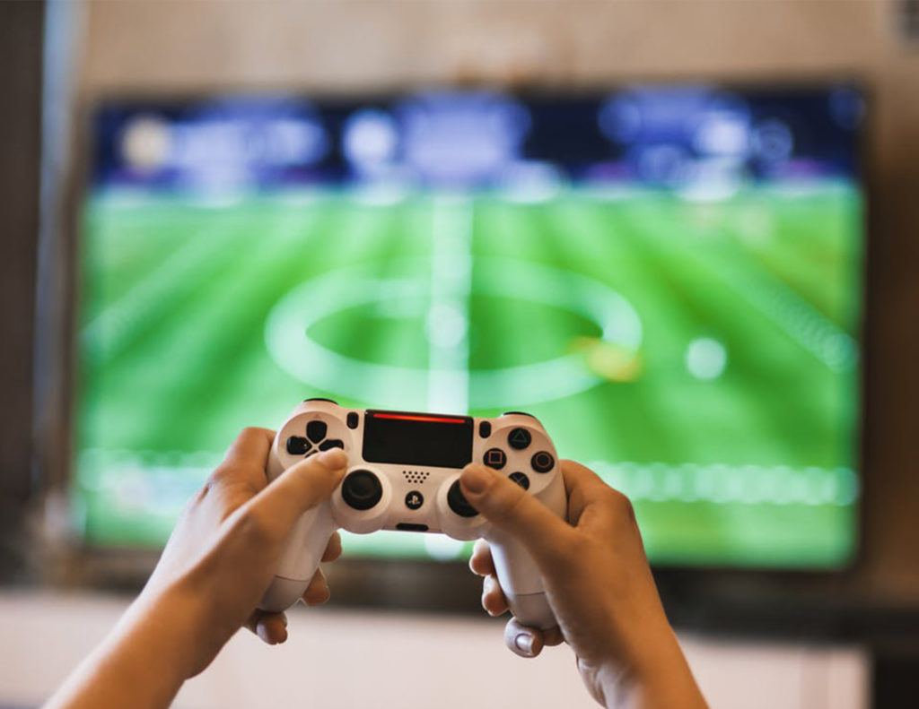 Football videogame on screen, hands holding controller in foreground