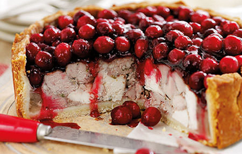 Deep, dense chicken and pork pie, one quarter cut, topped with glazed cranberries, red juice running down