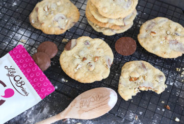 Freshly made choc chunk cookies on cooling rack with wooden spoon and extra choc buttons