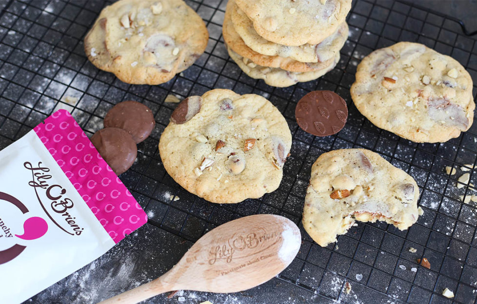 Freshly made choc chunk cookies on cooling rack with wooden spoon and extra choc buttons