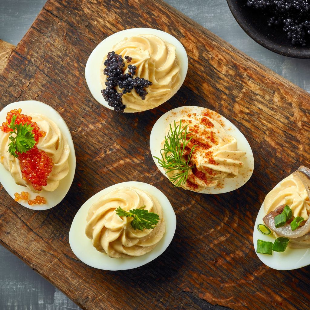 Devilled eggs, half boiled egg with yolk piped in a swirl and decorated with caviar and herb sprigs