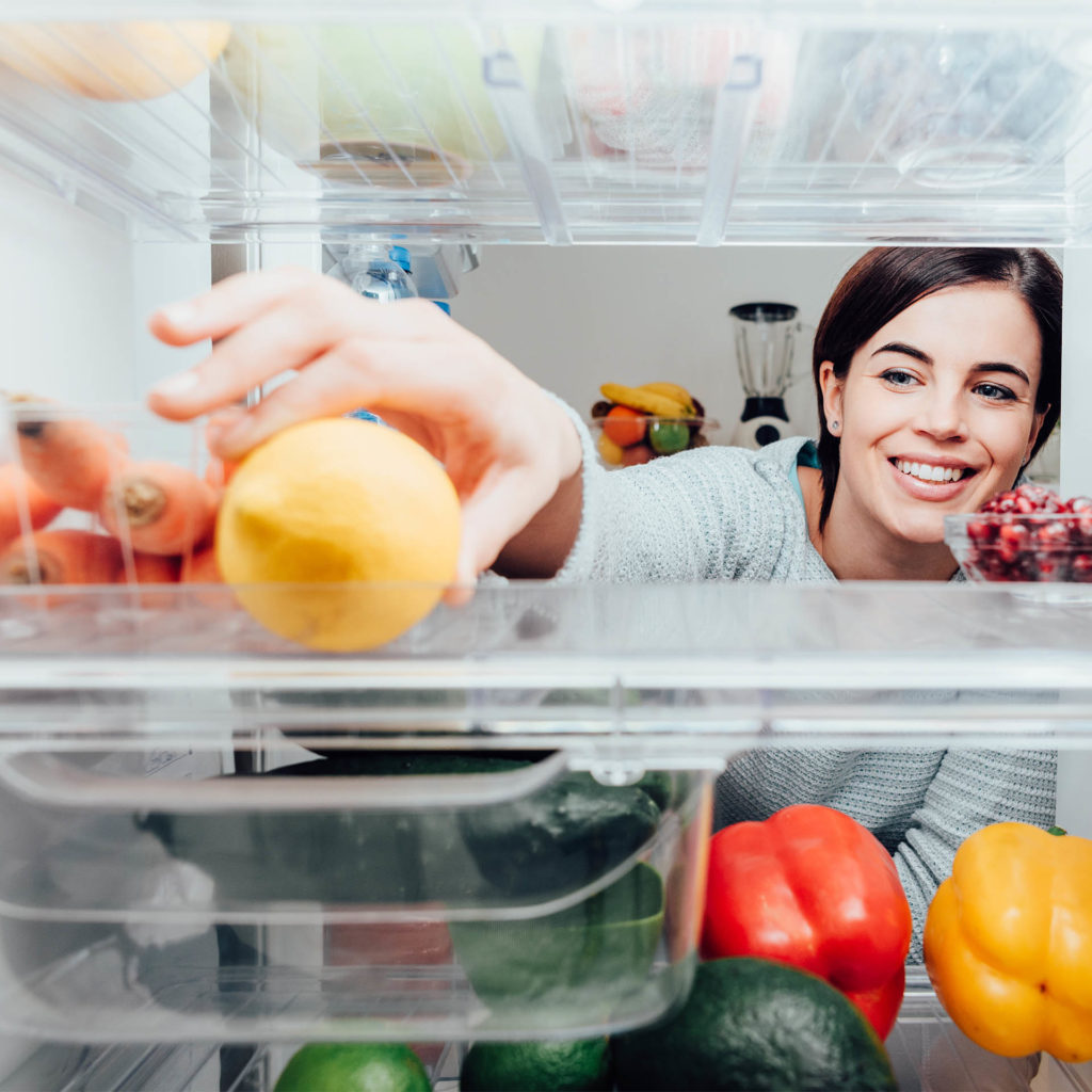 Woman reaching into fridge, putting fresh fruit at the back