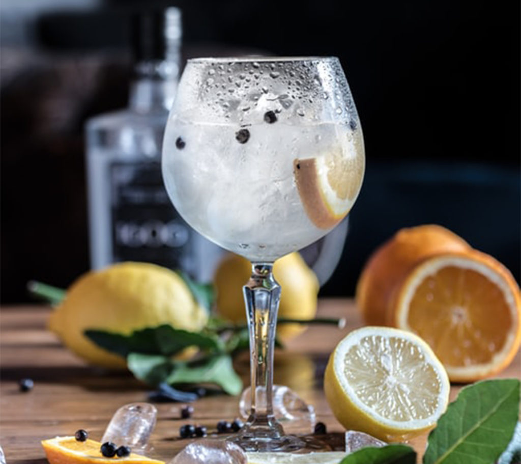 Large glass of gin with cut lemons, ice cubes and leaves scattered around