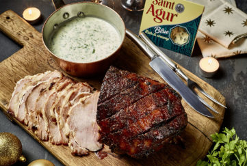 Brown caramelised glazed ham, cut into slices on wooden board, bowl of Saint Agur blue cheese dressing on the side