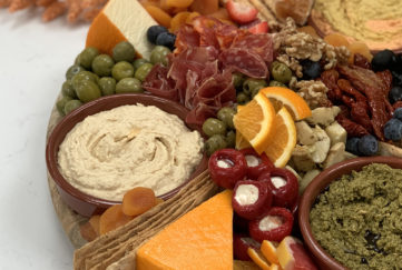 Grazing platter with olives, cured meat, cheese, stuffed peppers, orange slices and dishes of dip,