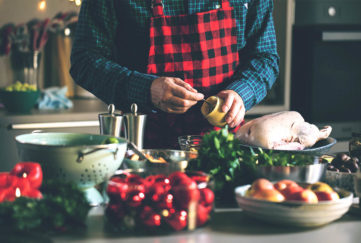 Middle aged man about to spread mustard on raw turkey, vegetables waiting to be prepared in foreground