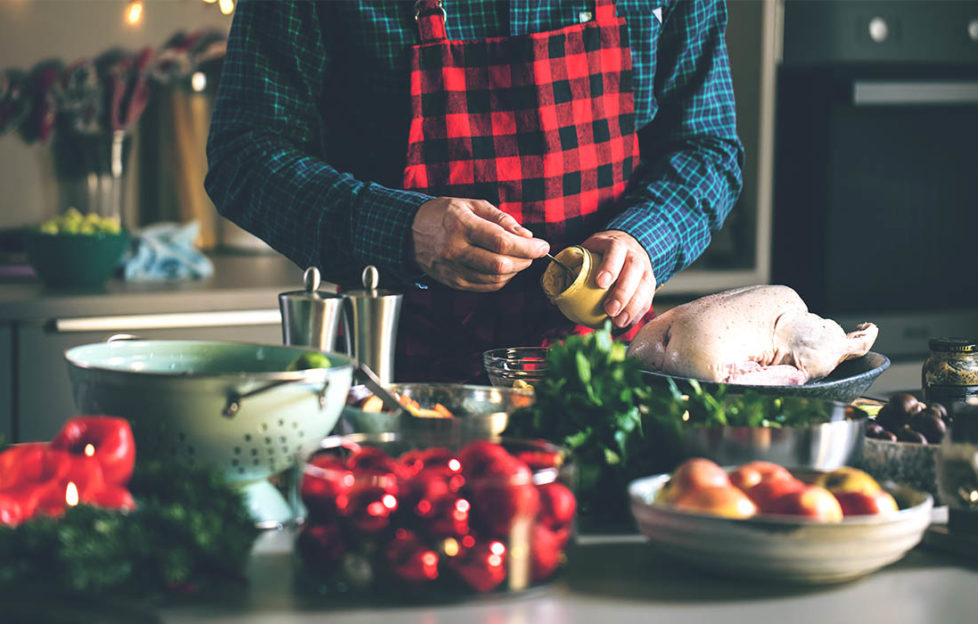 Middle aged man about to spread mustard on raw turkey, vegetables waiting to be prepared in foreground