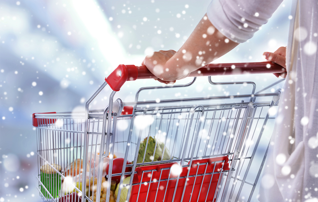 Save money on Christmas food shopping - woman pushing supermarket trolley, half full of Christmas food, snow falling