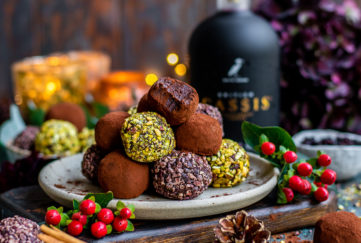 Plte of gorgeous truffles coated in pistachios and cocoa in a pyramid on a plate, one with a bite taken, berries, pine cones and cassis bottle