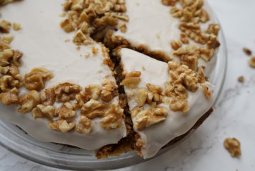 Carrot cake, one slice cut, decorated with creamy icing and crushed walnuts