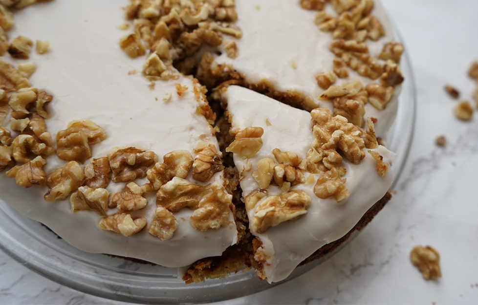 Carrot cake, one slice cut, decorated with creamy icing and crushed walnuts
