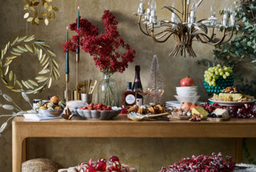 Table with plates of food, candles, decorative branches with berries, gold leaves and rustic light fitting