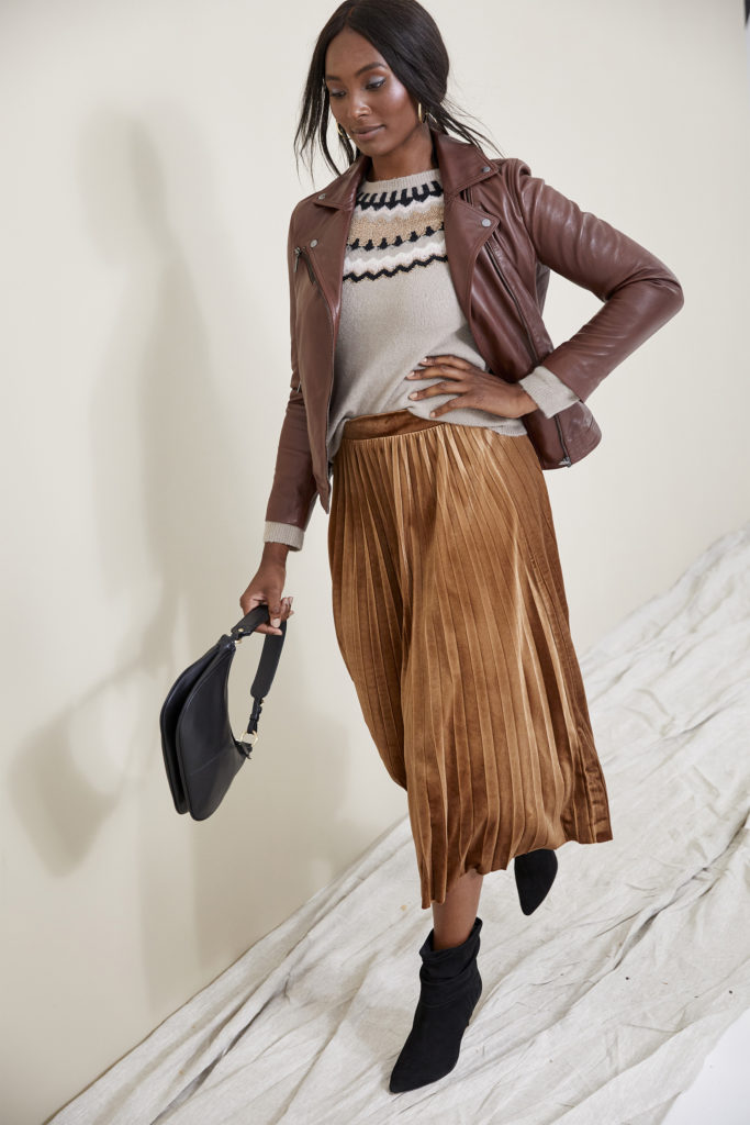 Model in dark tan waist length leather jacket over fair isle style jumper and long metallic bronze pleated skirt