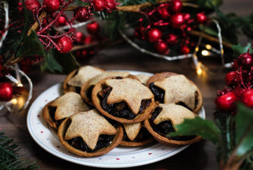 Plate of home made mince pies topped with pastry stars, red berry decorations behind