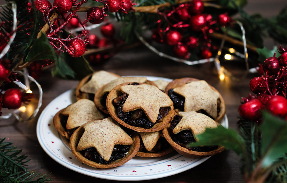 Plate of home made mince pies topped with pastry stars, red berry decorations behind