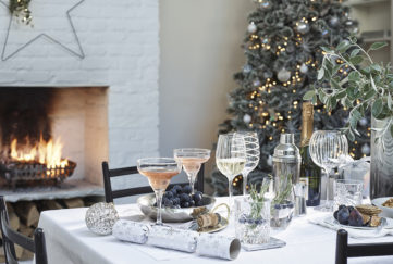 Table set for Christmas dinner with decorated wine glasses and crackers, frost themed Christmas tree behind