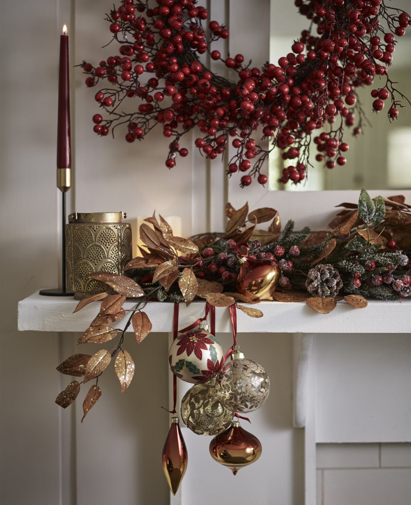 Mantelpiece with cranberry wreath, slim gold candle and selection of reddish gold leaves and baubles