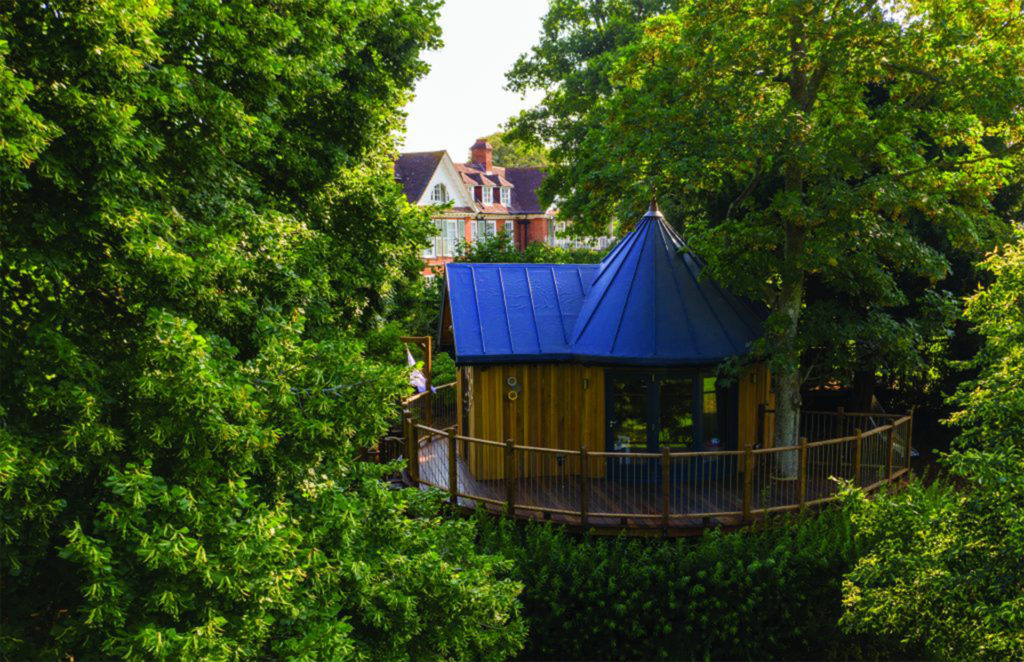 Blue roofed treehouse accommodation with circular platform, hotel beyond