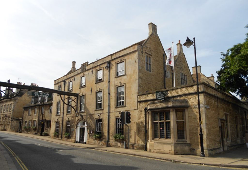 3 storey brown stone building with metal arch across the road bearing the hotel's name