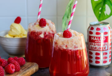 2 glasses of raspberry and beer cocktail topped with ice cream and a raspberry, striped drinking straws