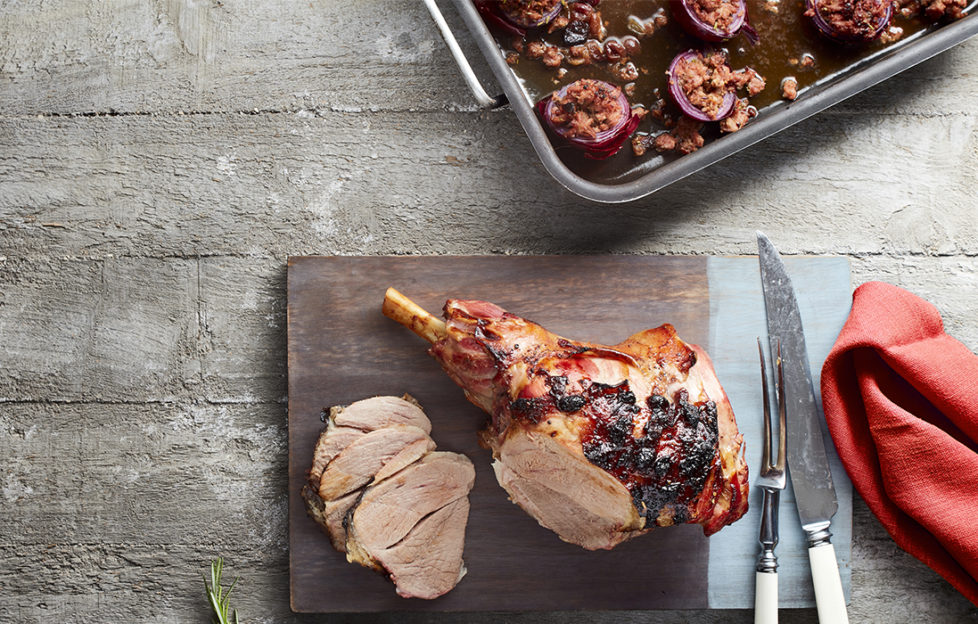 roast leg of lamb being carved, roasting tin with stufed onions and deep red cranberry/gin sauce