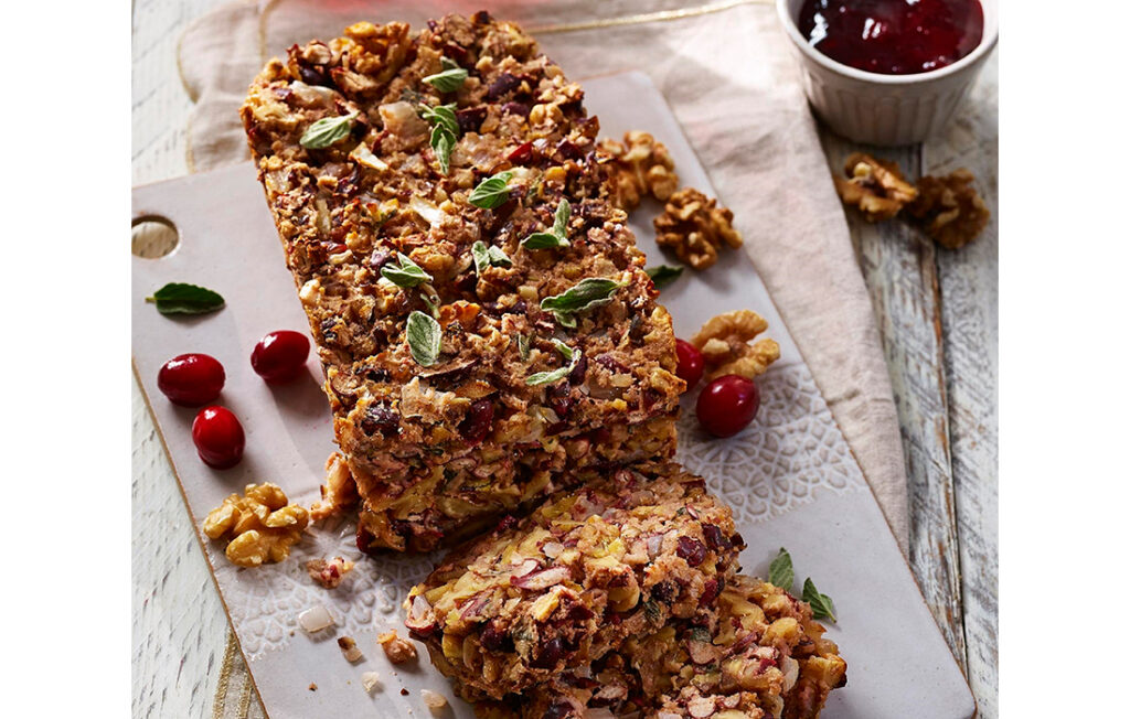 Nut loaf cut in slices with pot of cranberry sauce and fresh cranberries and sage leaves